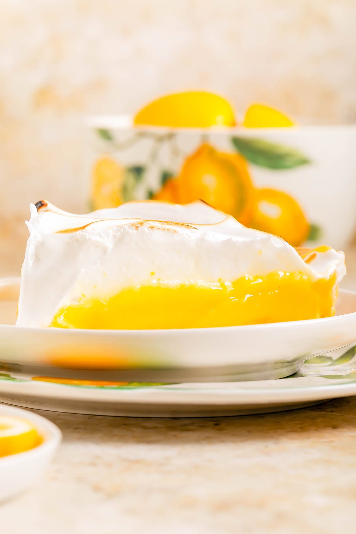 A slice of lemon meringue pie with a golden-yellow filling and fluffy meringue topping sits on a decorative plate.