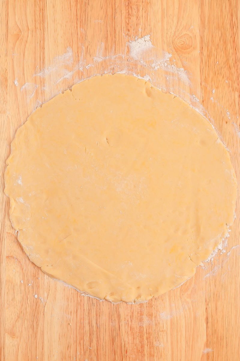 A large, round sheet of rolled-out dough rests on a lightly floured wooden surface.