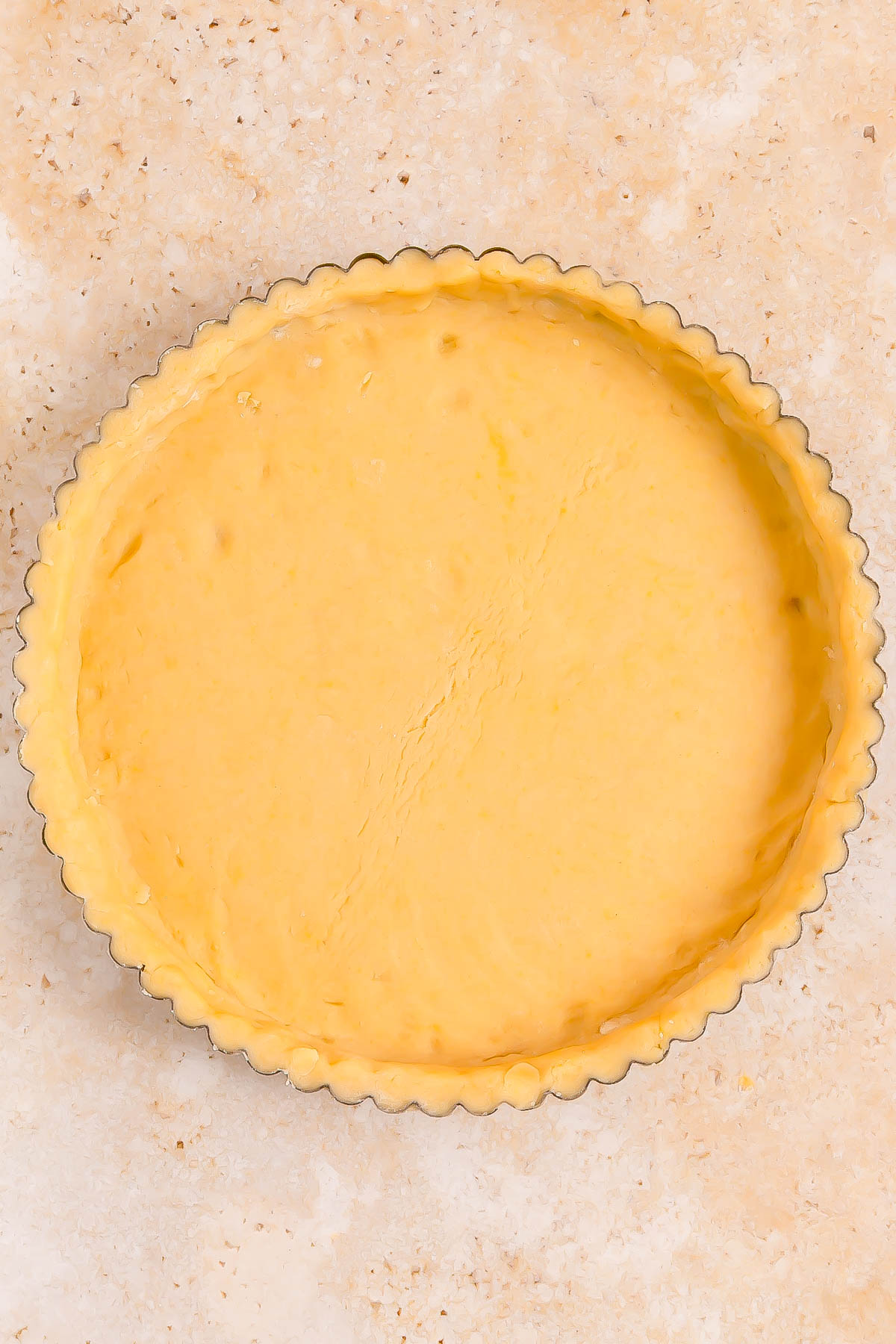 Unbaked, empty pie crust evenly pressed into a fluted tart pan on a light marble surface.