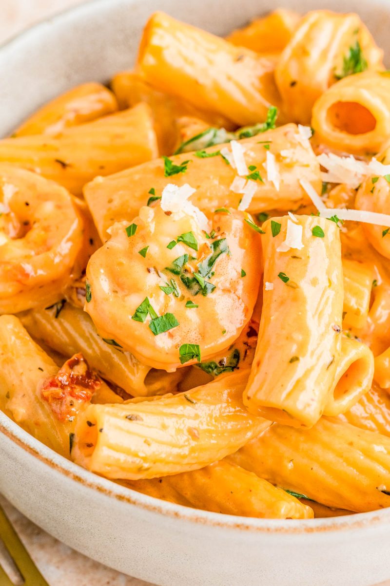 A bowl of creamy rigatoni pasta with shrimp, topped with chopped parsley and shredded cheese.