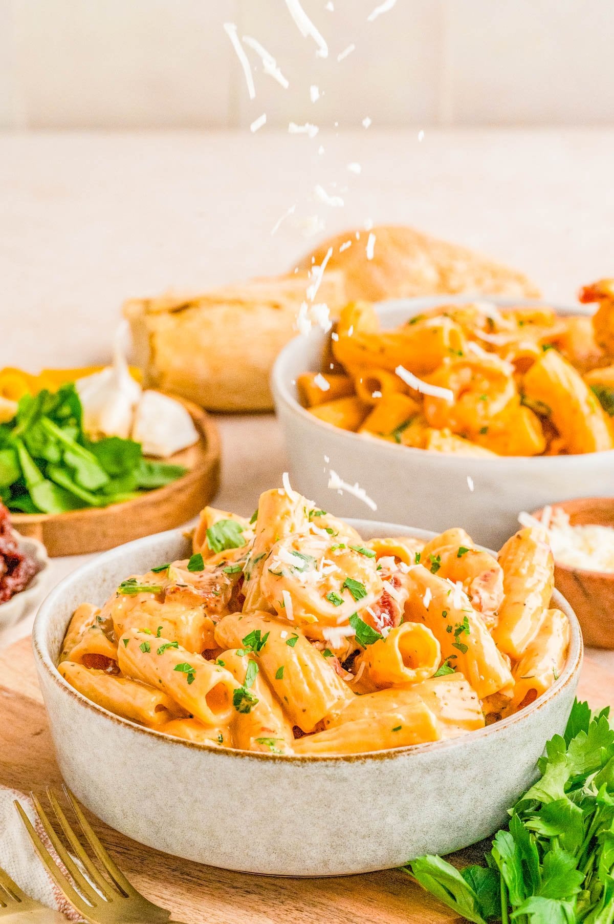 Bowl of creamy pasta garnished with parsley and grated cheese, with bread, salad, and parsley in the background on a wooden board.