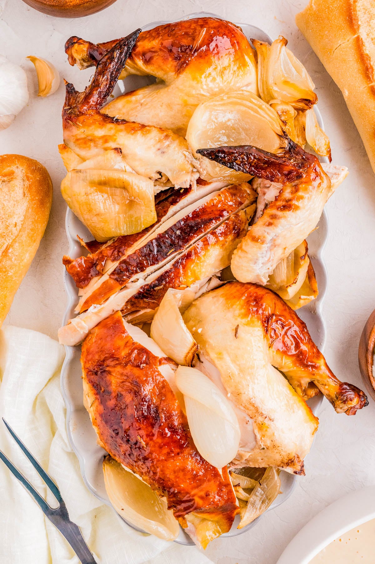 Roast chicken cut into pieces and served with roasted onions on a white platter, surrounded by bread and utensils.