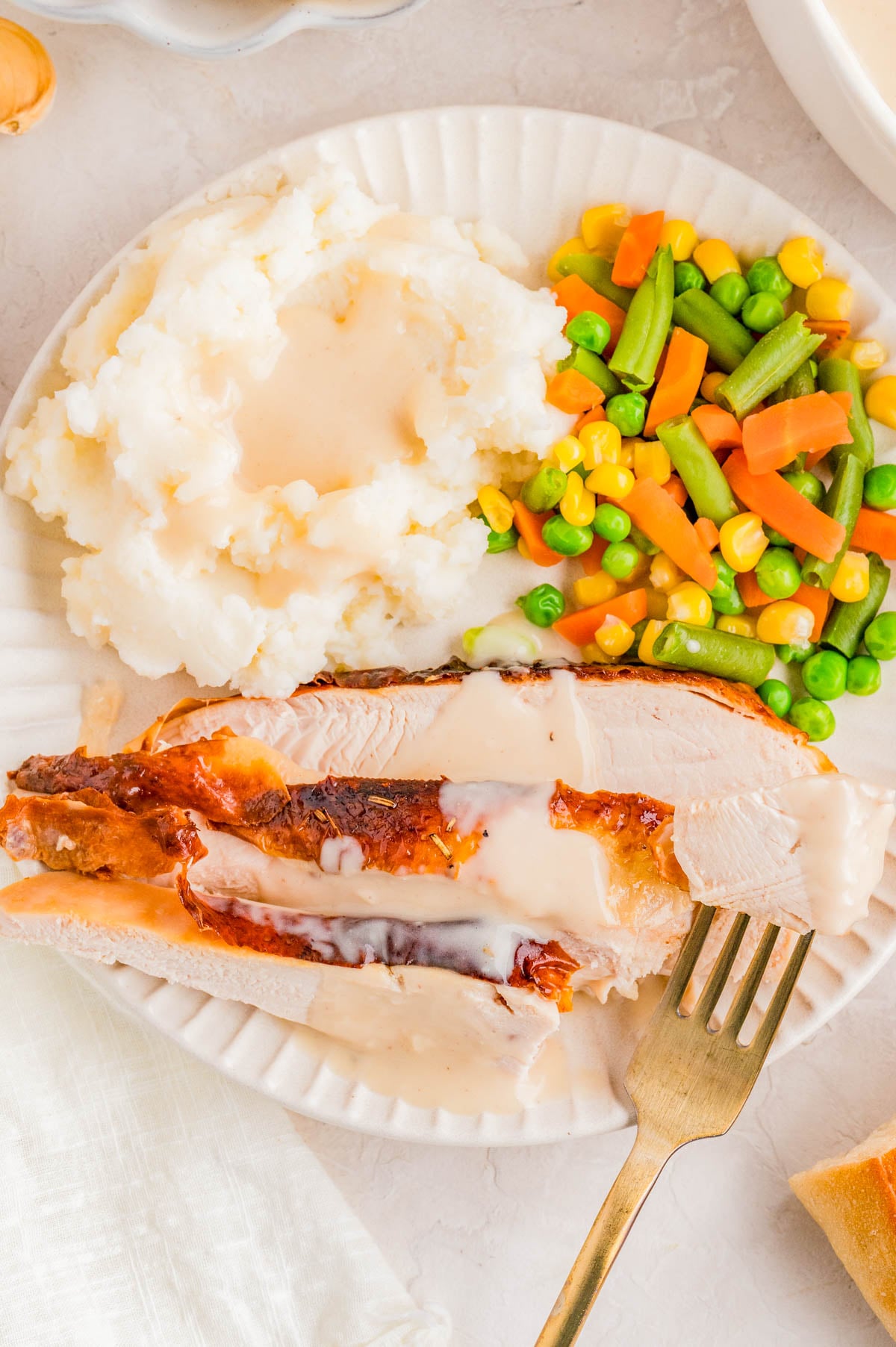 A plate with sliced roast turkey topped with gravy, mashed potatoes with more gravy, and mixed vegetables including carrots, corn, peas, and green beans.