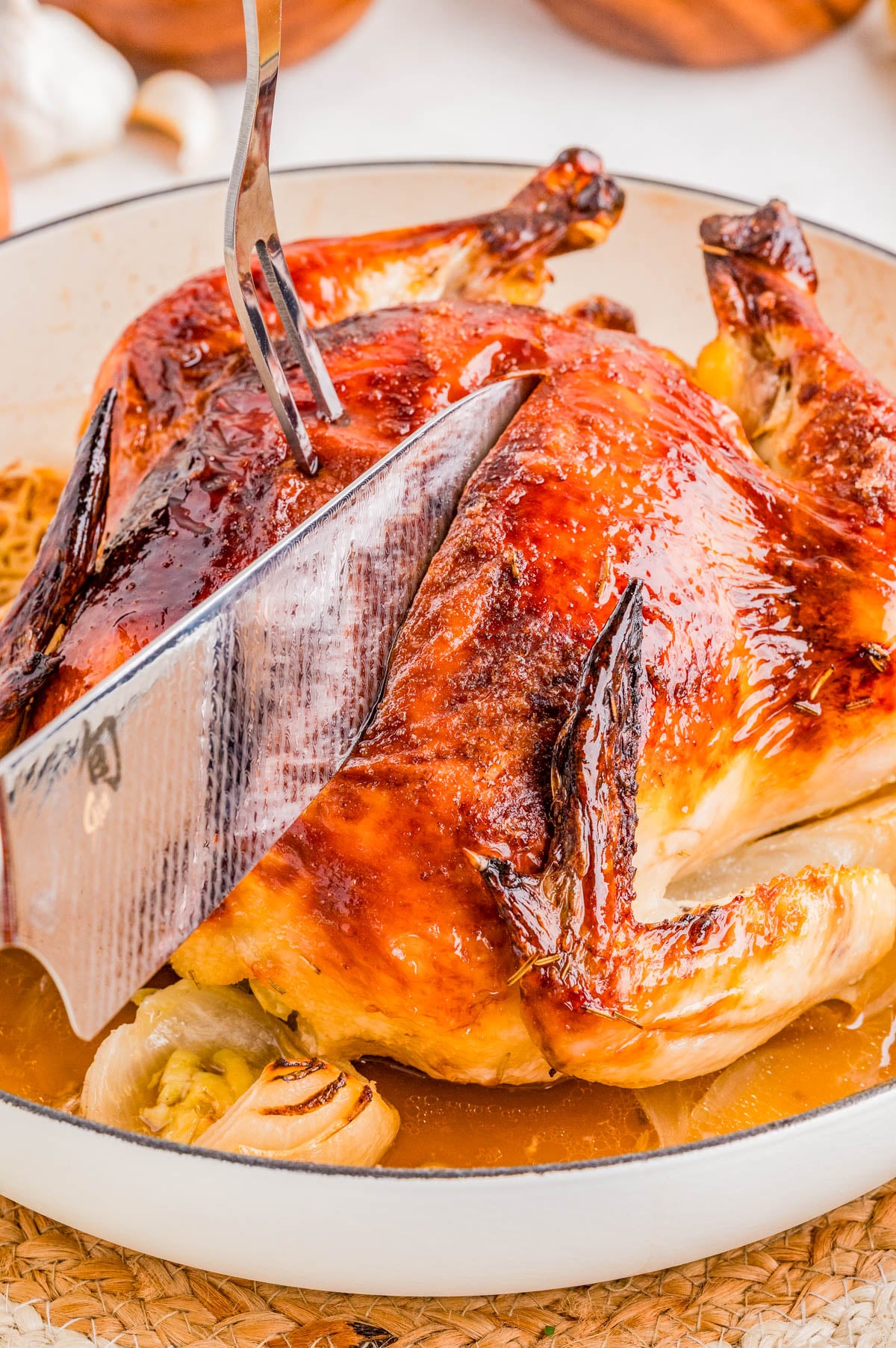 A person slices a roasted whole chicken with a knife and fork in a white dish.