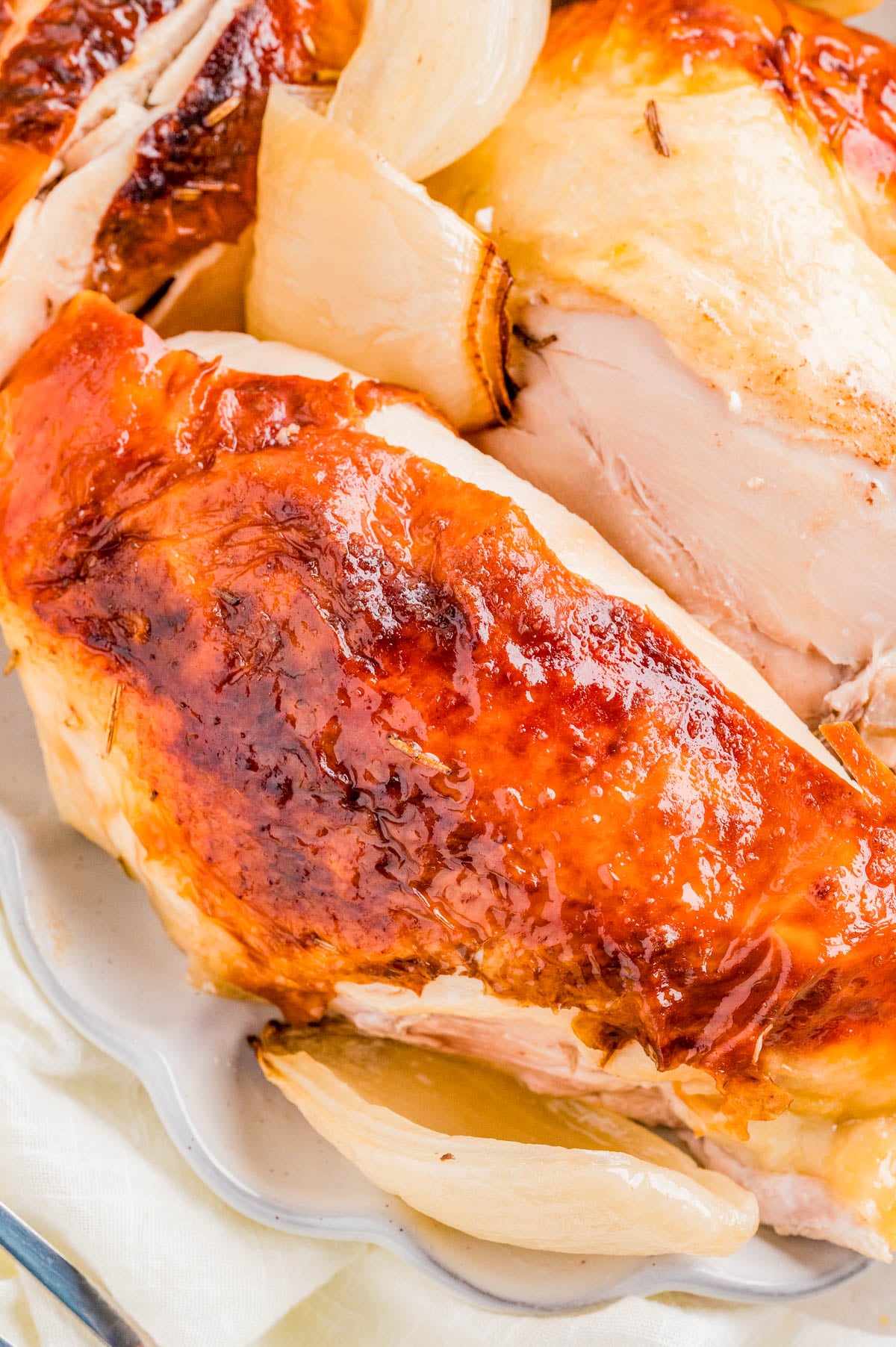 Close-up of roasted chicken with golden brown skin and roasted onion pieces on a white plate.