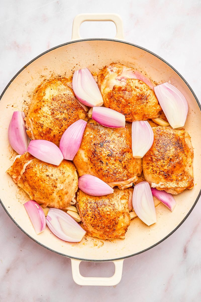 A round baking dish with six seasoned chicken thighs and chopped red onions arranged on a light surface.
