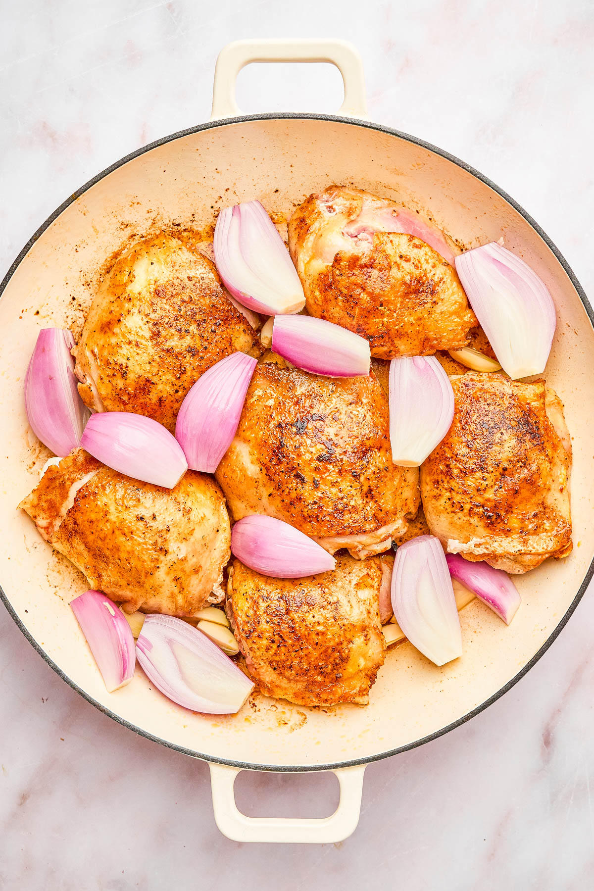 A round baking dish with six seasoned chicken thighs and chopped red onions arranged on a light surface.