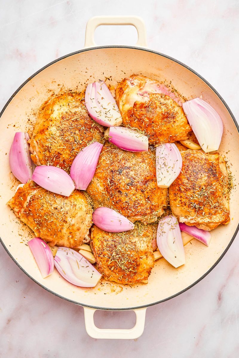 A round baking dish filled with seasoned, cooked chicken thighs and chunks of red onion on a light countertop.