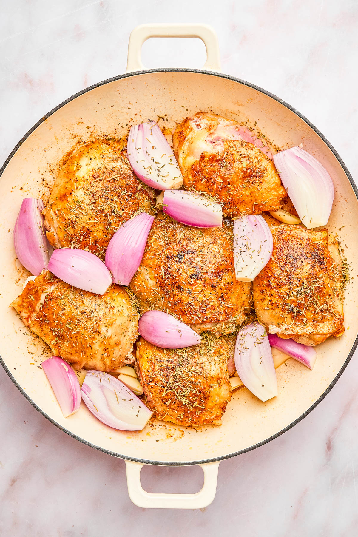 A round baking dish filled with seasoned, cooked chicken thighs and chunks of red onion on a light countertop.