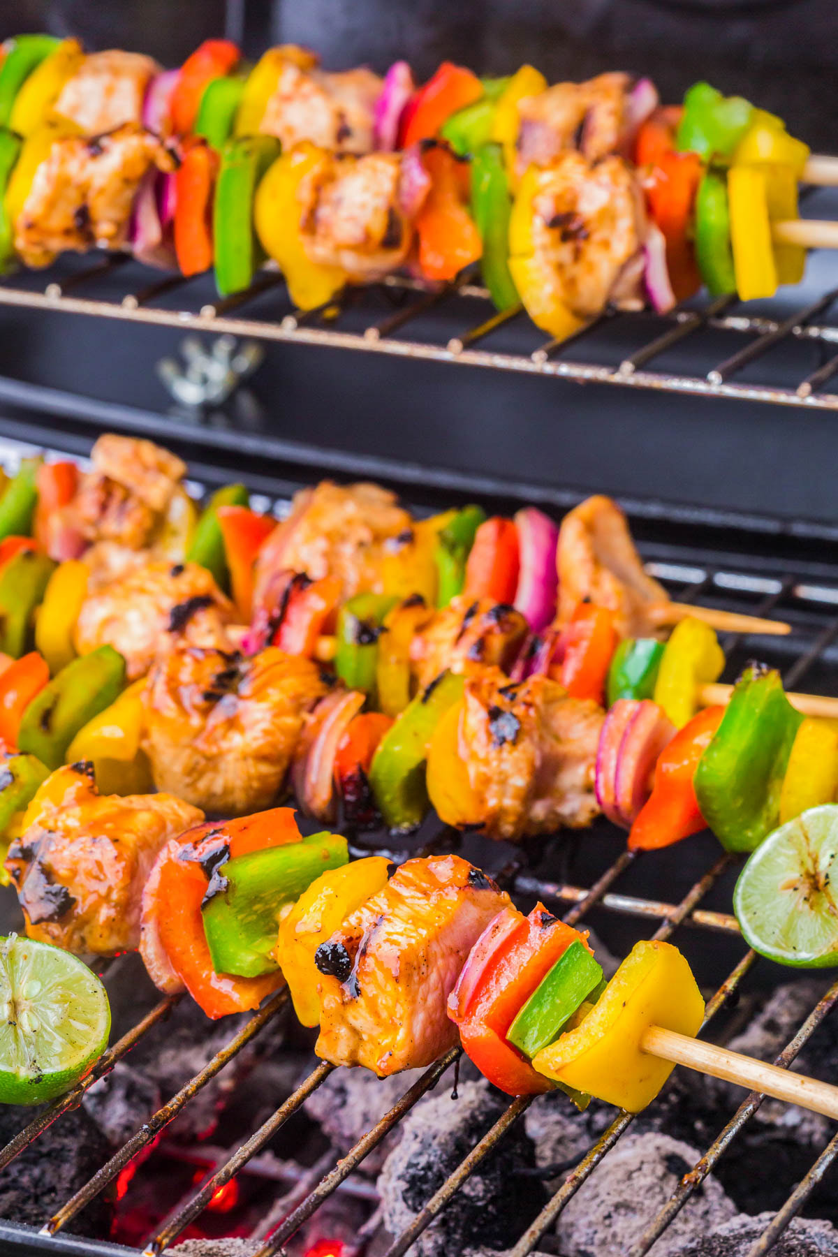 Colorful chicken and vegetable skewers grilling over charcoal, with pieces of bell pepper, onion, and lime slices visible.