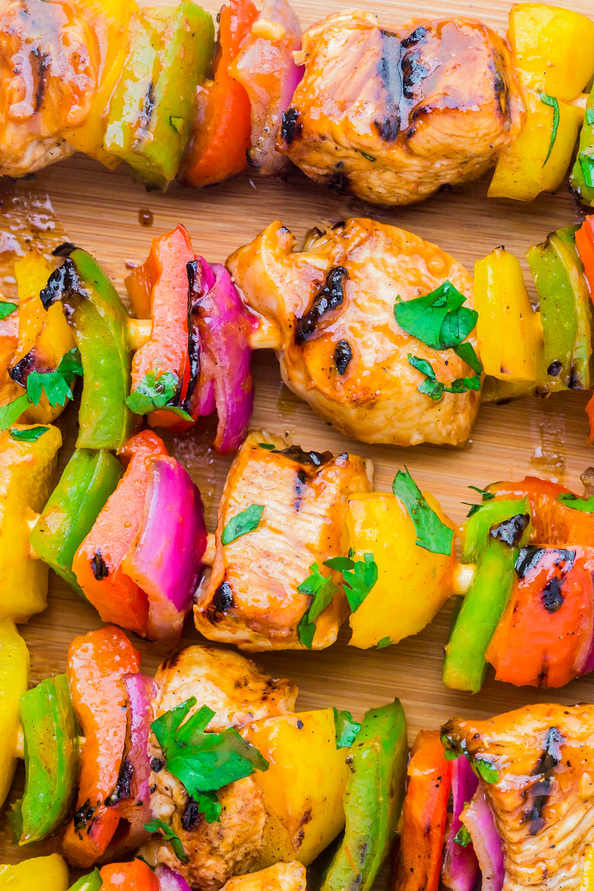Close-up of grilled kebabs with pieces of chicken, red and green bell peppers, yellow peppers, and red onions garnished with chopped parsley on a wooden surface.