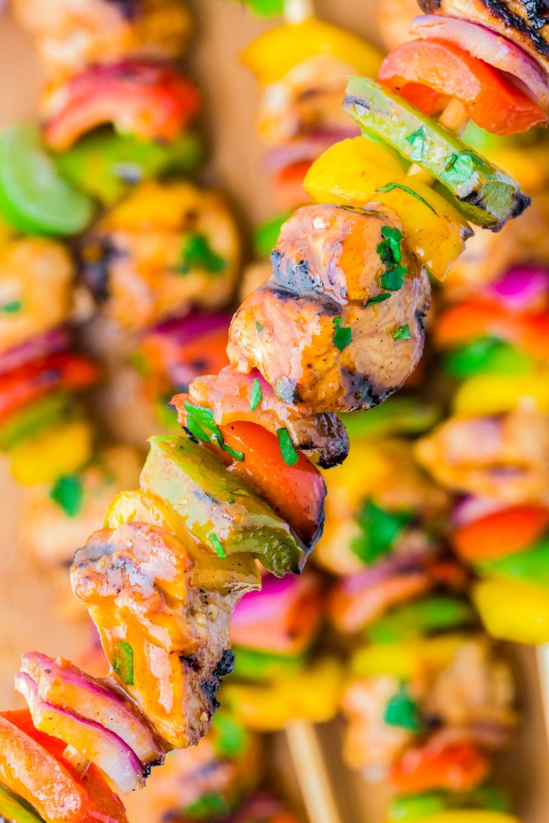 Colorful grilled kebabs with pieces of marinated meat, bell peppers, onions, and herbs on wooden skewers.