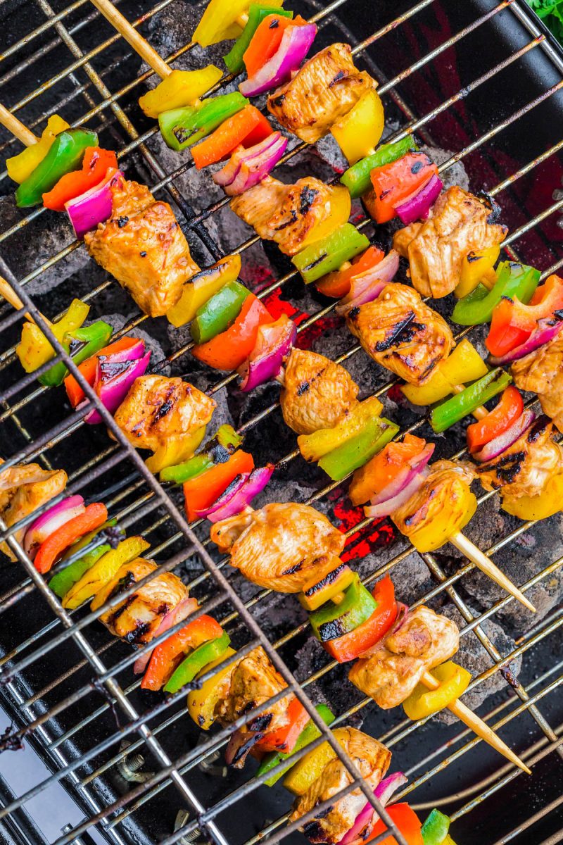 Colorful chicken and vegetable skewers, including bell peppers and red onions, grilling on a barbecue over hot coals.