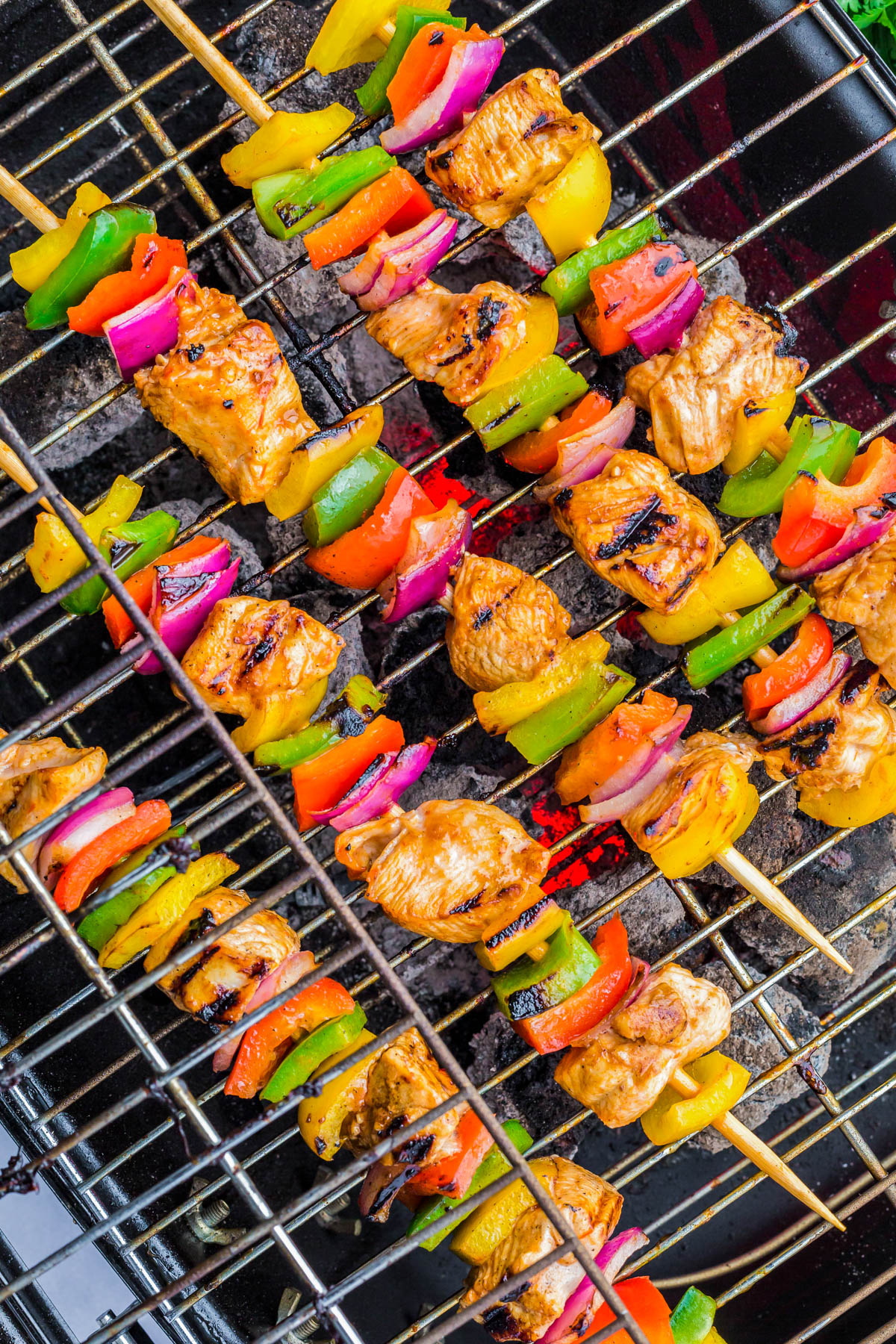 Colorful chicken and vegetable skewers, including bell peppers and red onions, grilling on a barbecue over hot coals.