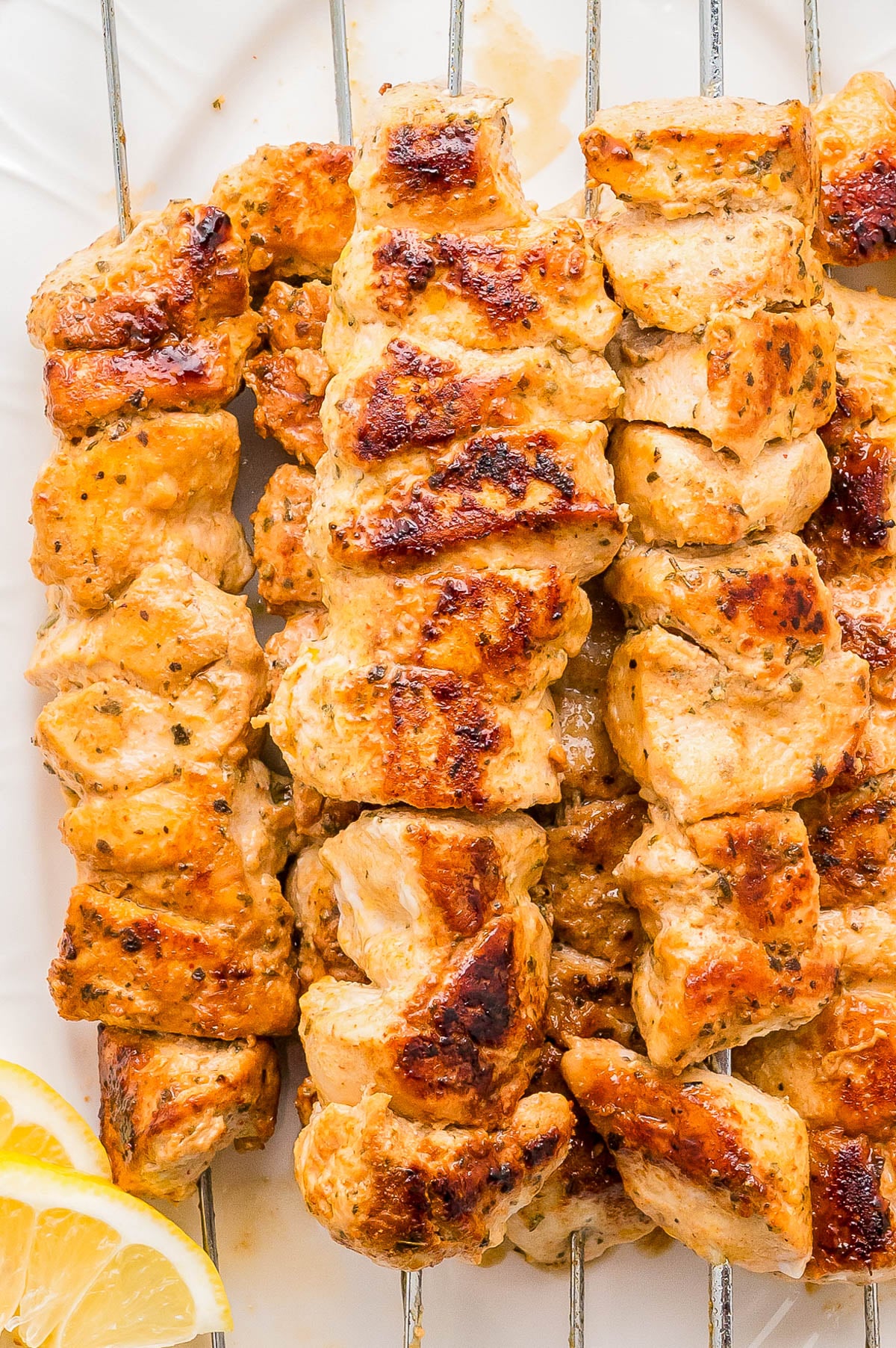 Grilled chicken skewers with a golden-brown char, served on metal skewers with lemon wedges on the side.