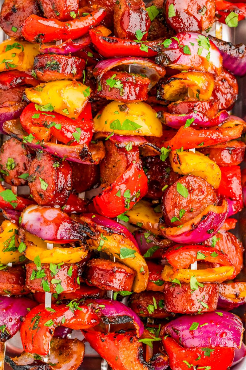 Grilled skewers with sliced sausage, red and yellow bell peppers, and red onions, garnished with chopped parsley.