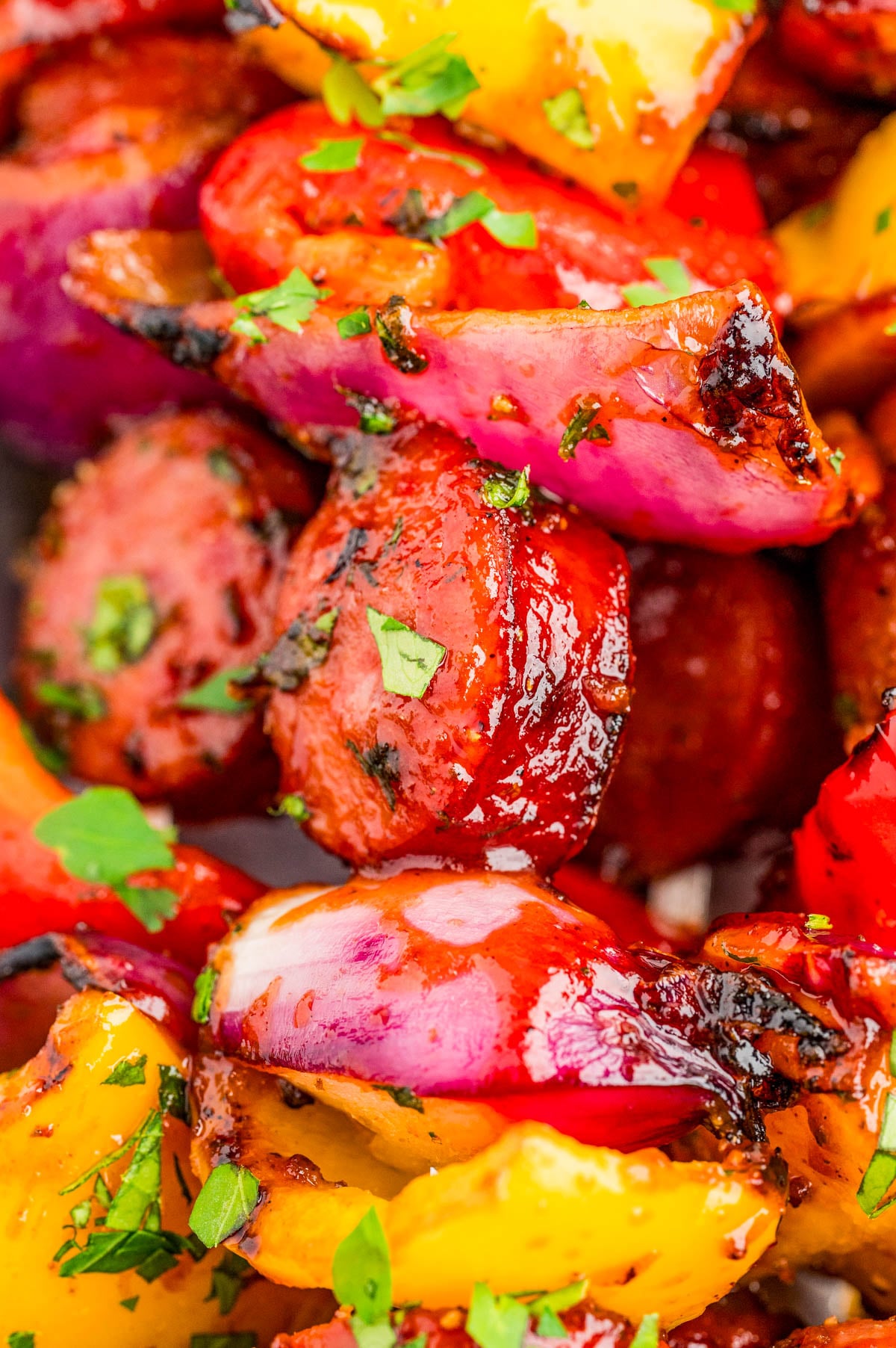 Close-up of grilled sausage slices, red onions, and yellow bell peppers garnished with chopped parsley.