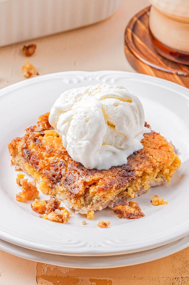A piece of crumbly cake topped with a scoop of vanilla ice cream is served on a white plate.