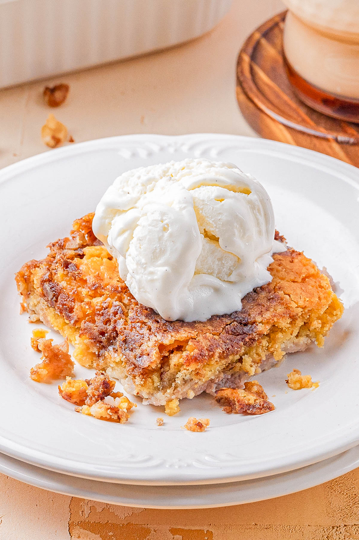 A piece of crumbly cake topped with a scoop of vanilla ice cream is served on a white plate.