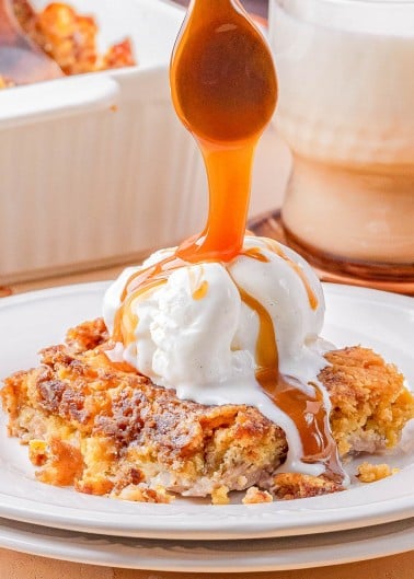 A serving of dessert topped with a scoop of vanilla ice cream, being drizzled with caramel sauce, is plated in front of a glass of milk.
