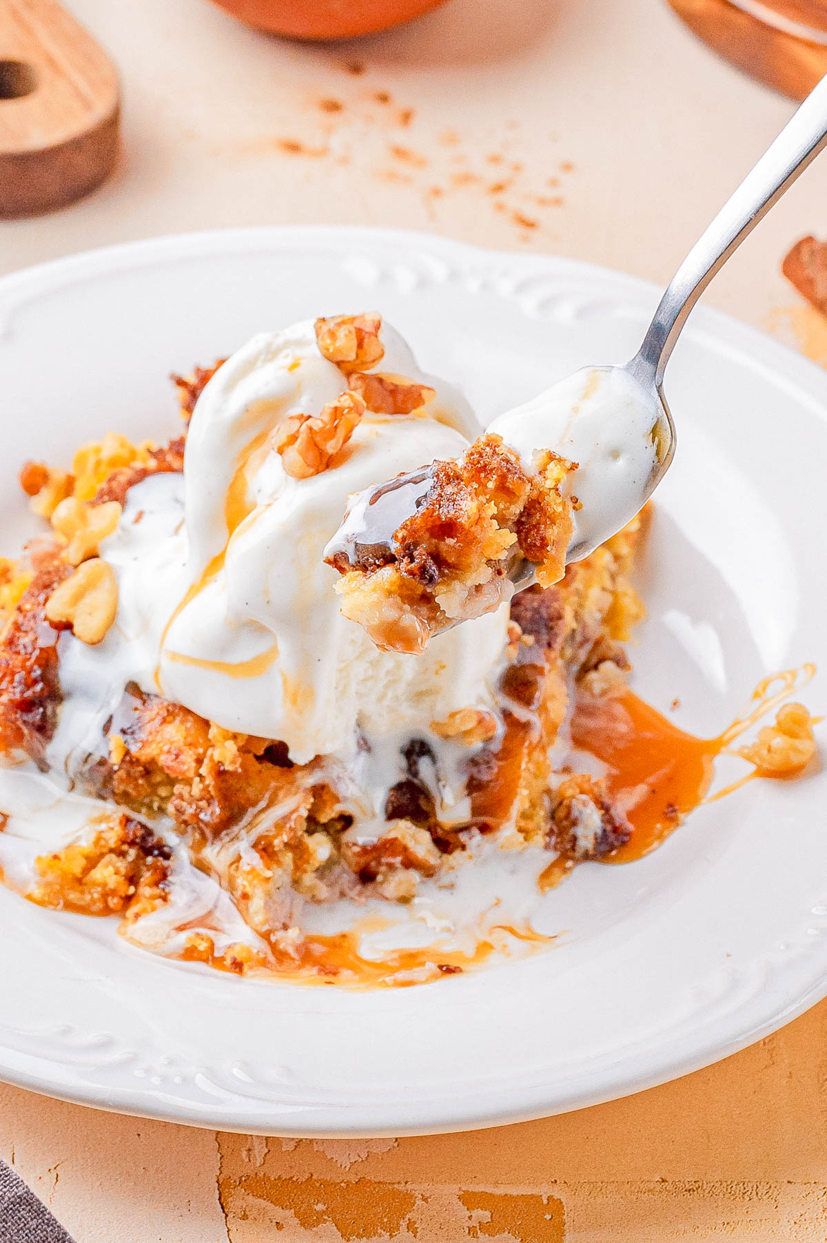 A close-up of a dessert topped with vanilla ice cream, caramel sauce, and chopped nuts, with a fork holding a bite above the plate.