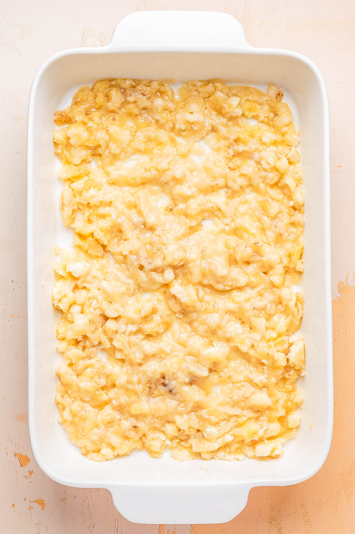 A white rectangular baking dish filled with a layer of mashed bananas spread evenly over the bottom.