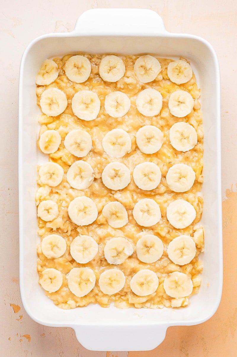 A white baking dish containing a layer of mashed bananas topped with evenly arranged banana slices.