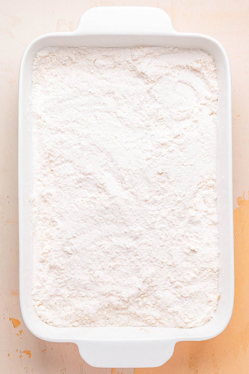 A white rectangular baking dish filled with an even layer of powdered white flour on a light-colored surface.