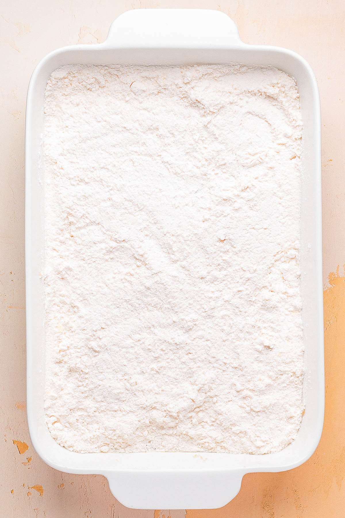 A white rectangular baking dish filled with an even layer of powdered white flour on a light-colored surface.