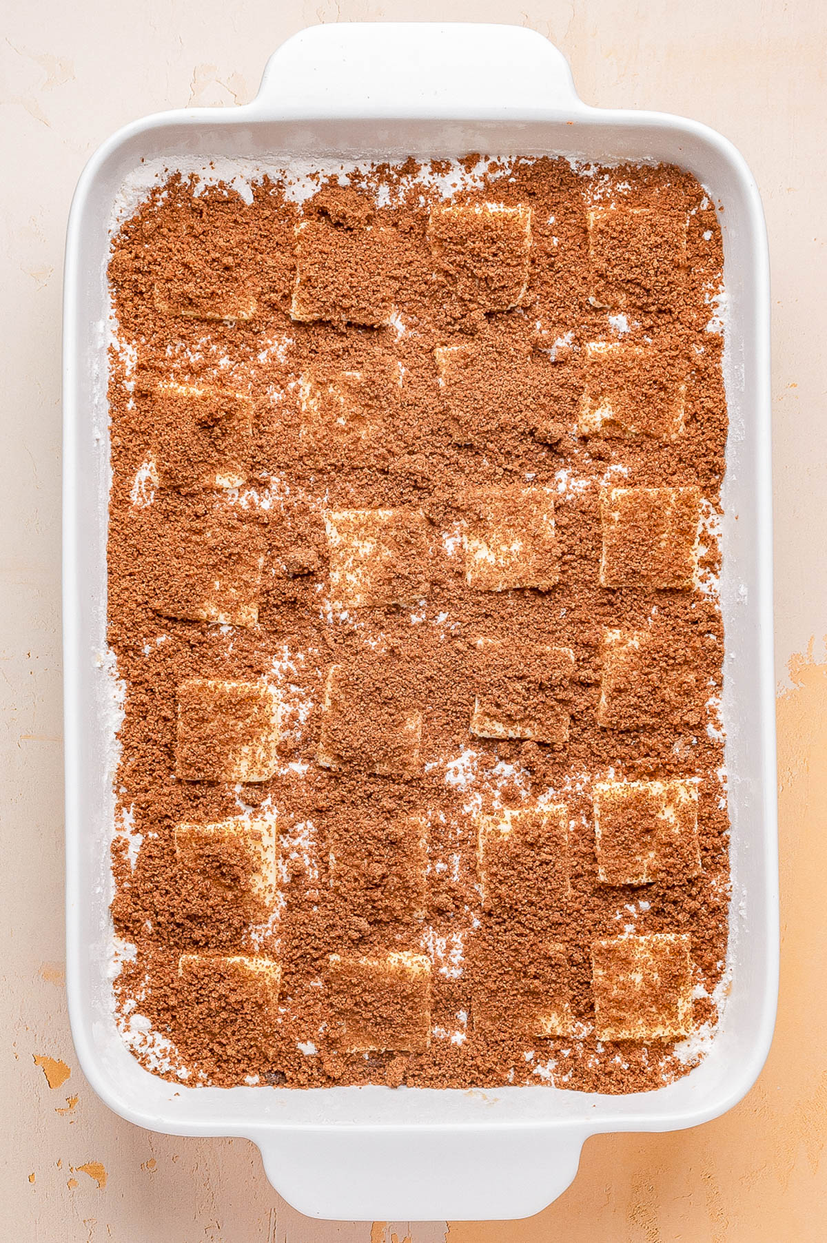 A white baking dish filled with layered rectangular pieces dusted with a generous amount of brown cinnamon sugar mixture.
