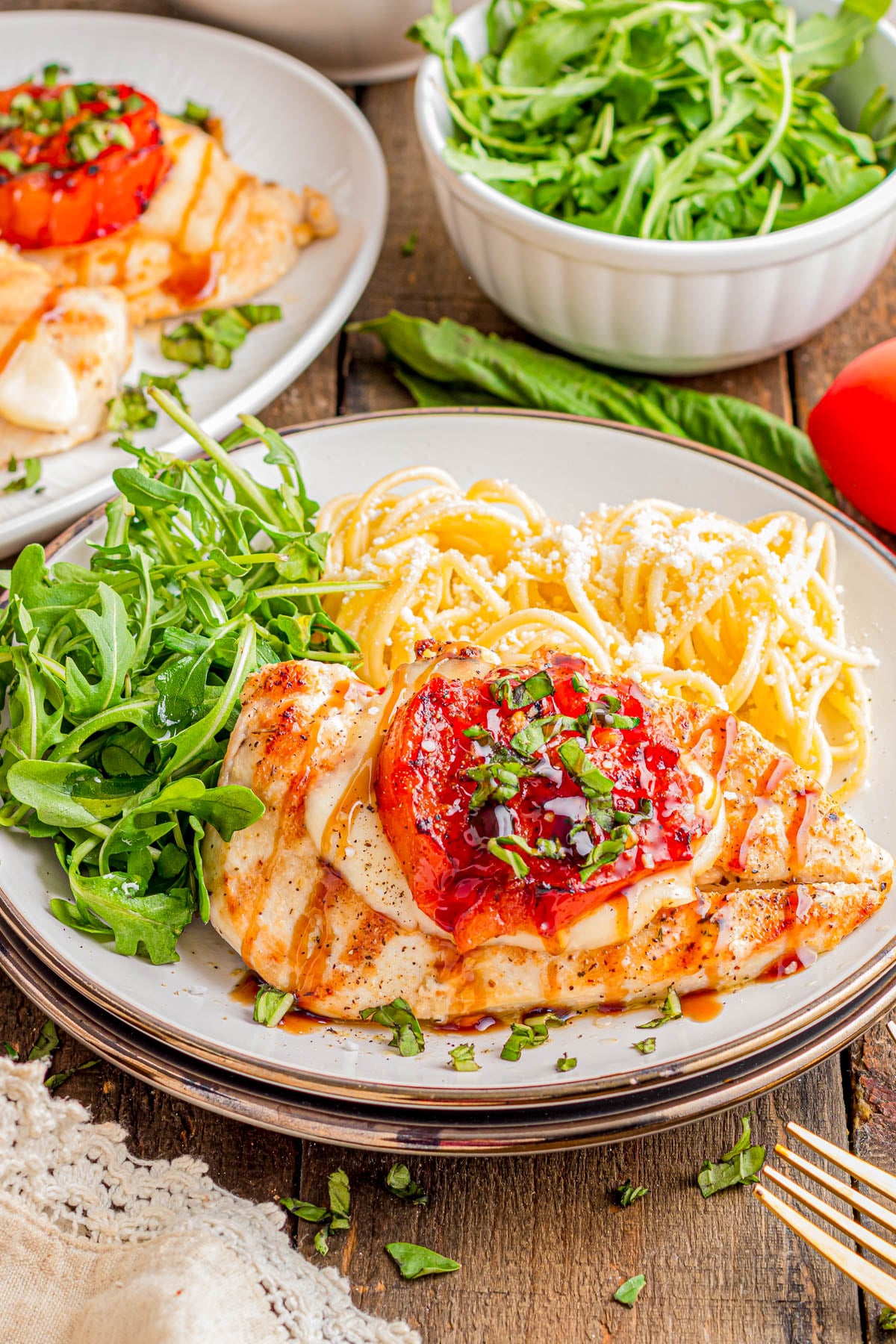 Grilled chicken breast topped with tomato and herbs, served with arugula and a portion of spaghetti on a white plate.