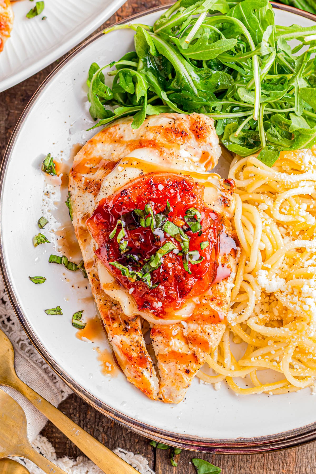 Grilled chicken breast topped with tomato sauce and herbs, served with spaghetti and grated cheese, and a side of fresh arugula on a white plate.