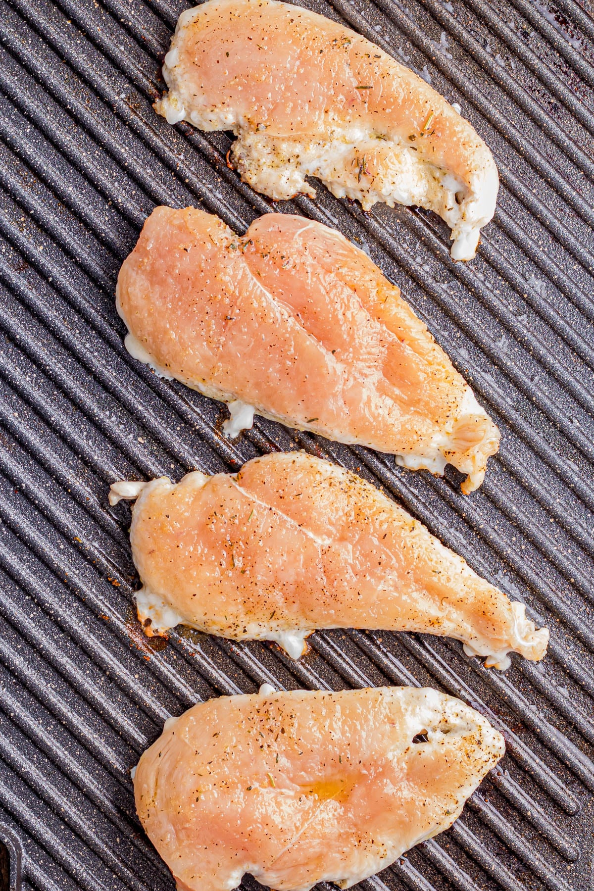 Four raw, seasoned chicken breast fillets on a ridged grill pan.