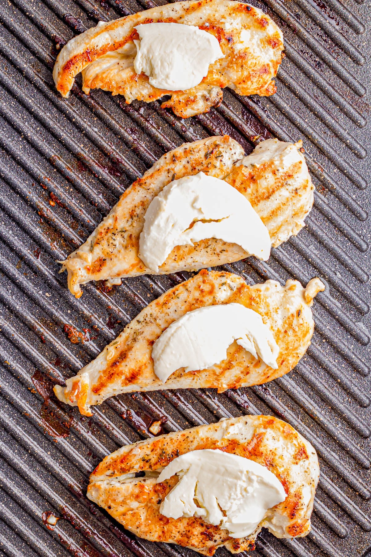 Four grilled chicken breasts topped with slices of mozzarella cheese cooking on a ribbed grill pan.