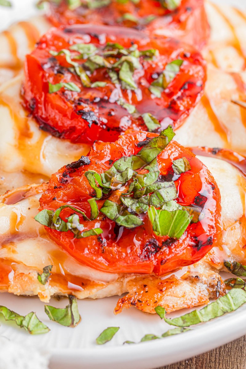 Close-up of a dish featuring roasted tomato slices topped with chopped fresh basil and a drizzle of balsamic glaze on melted cheese.