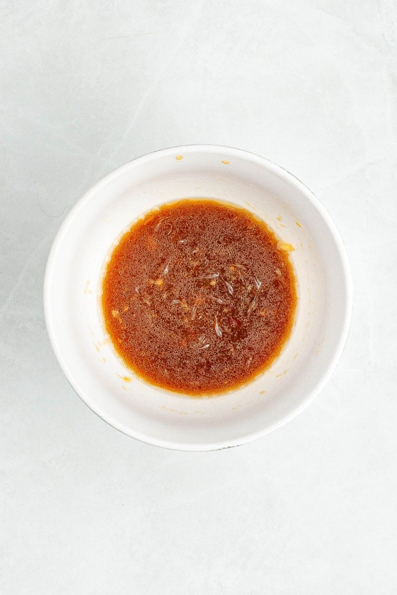 A white bowl containing a small amount of brown liquid sauce on a light-colored surface.