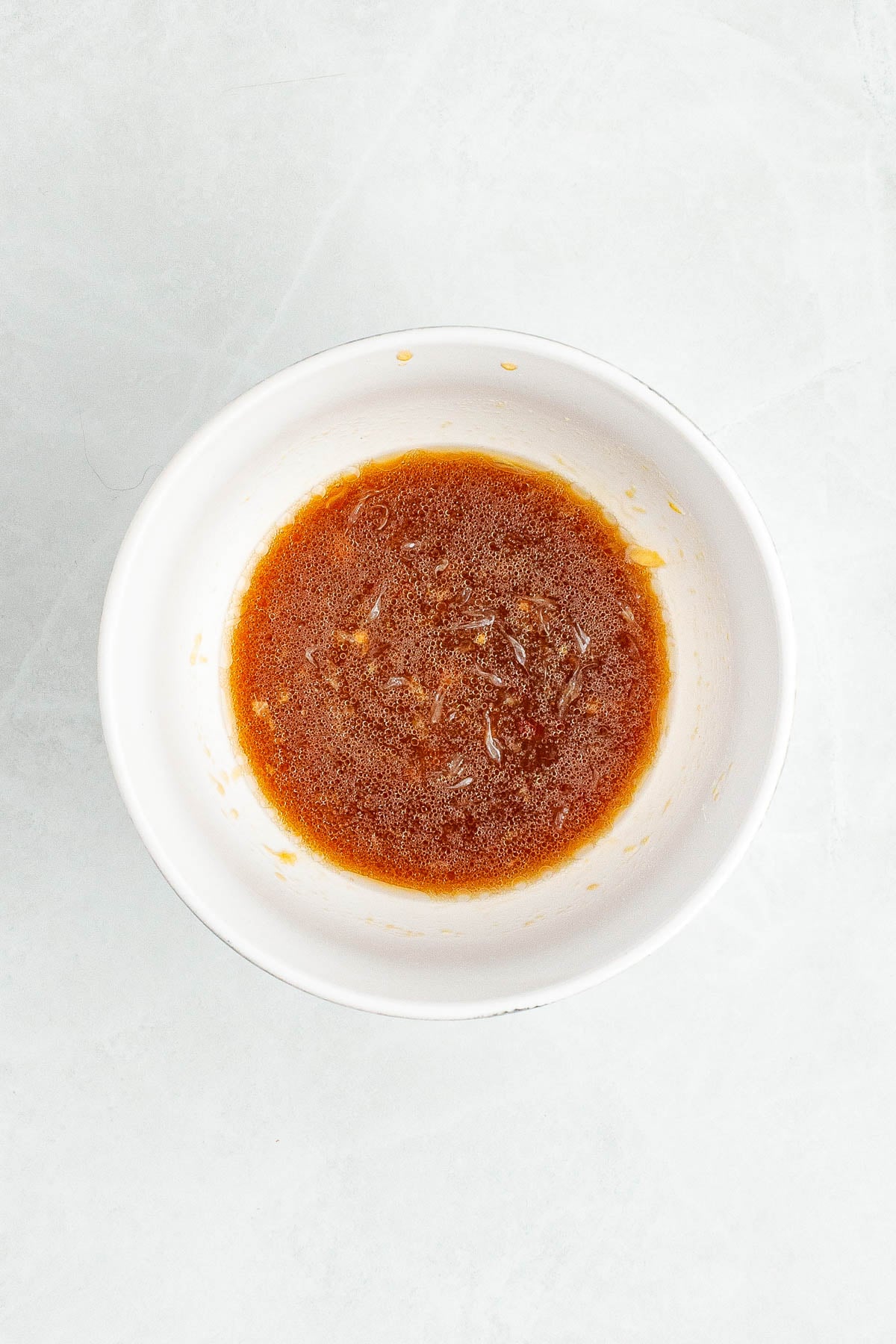 A white bowl containing a small amount of brown liquid sauce on a light-colored surface.