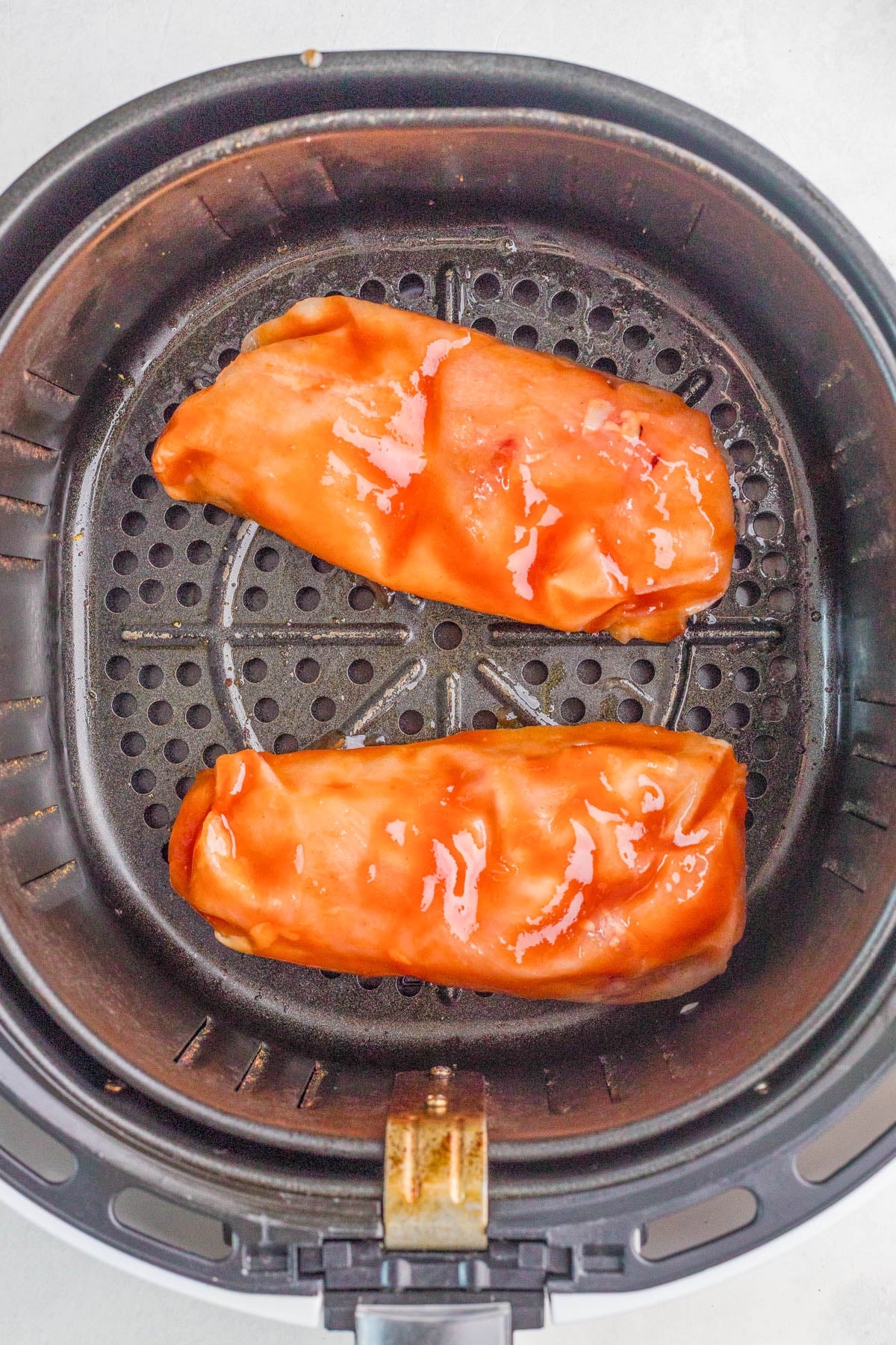 Two sauced burritos are placed side by side inside an air fryer basket, ready to be cooked.