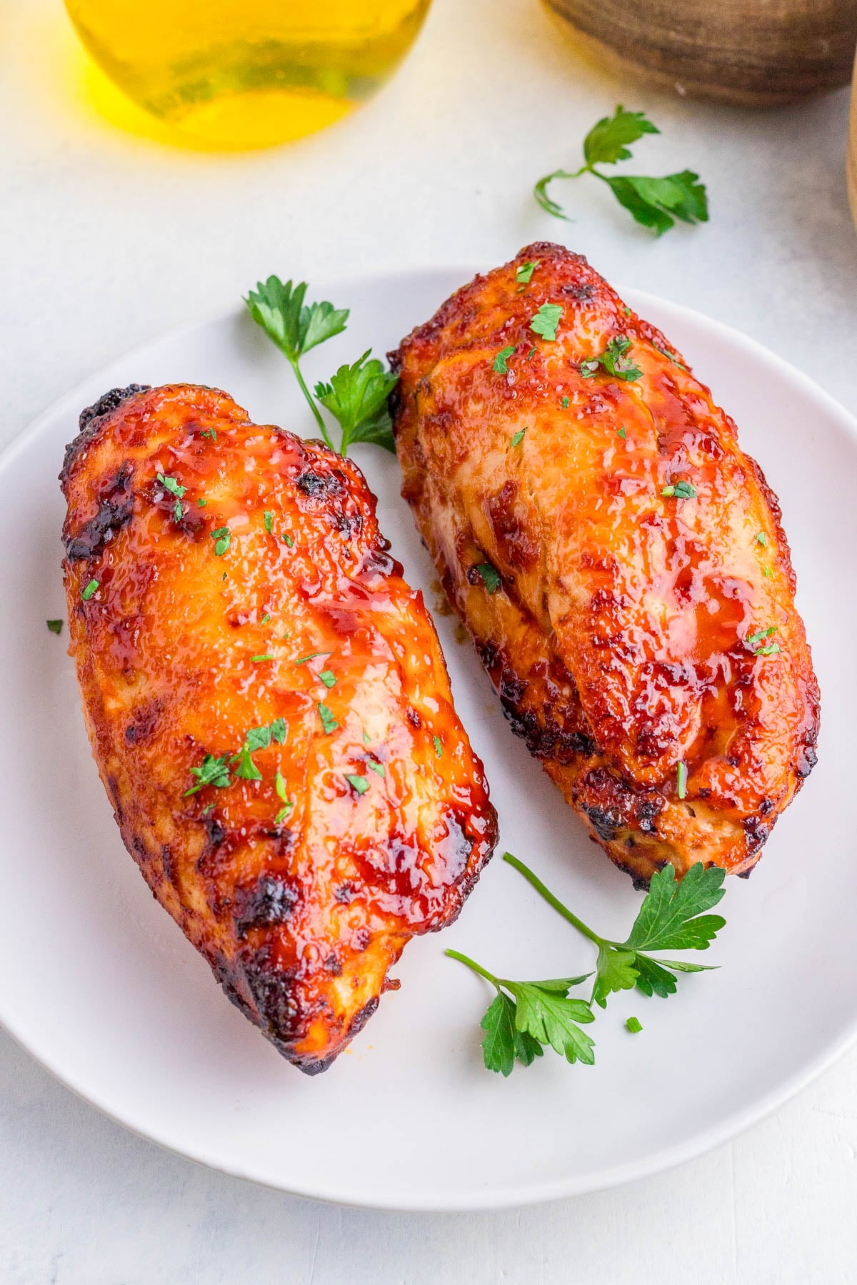 Two glazed, roasted chicken breasts garnished with chopped parsley on a white plate, with parsley sprigs as decoration.