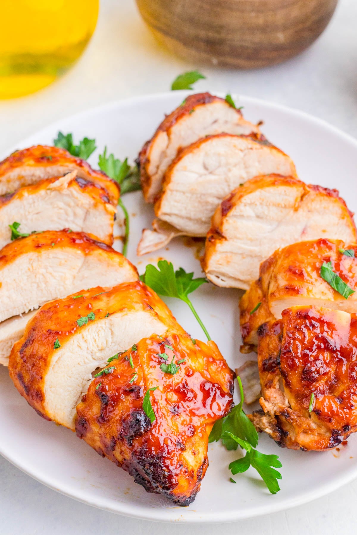 Sliced grilled chicken breasts with a glazed sauce and parsley garnish are arranged on a white plate.