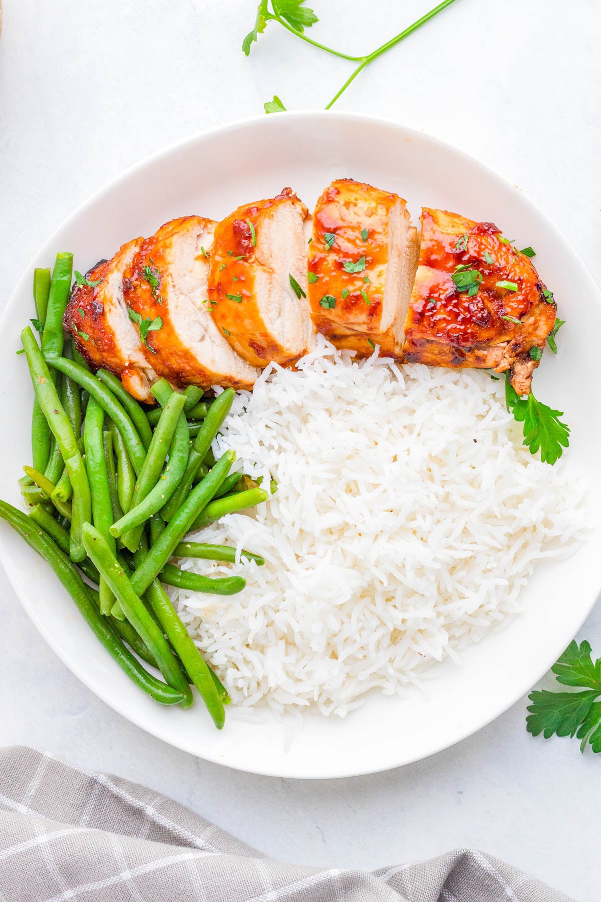 White plate with sliced grilled chicken breast, steamed green beans, and a serving of white rice, garnished with fresh parsley.