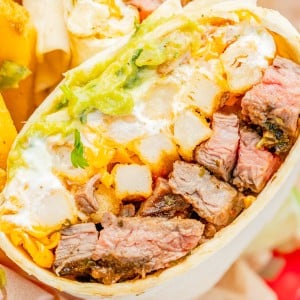A close-up of a burrito cut in half, showing steak, cheddar cheese, guacamole, sour cream, and potato pieces in a flour tortilla.