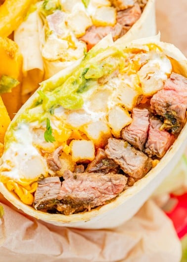 A close-up of a burrito cut in half, showing steak, cheddar cheese, guacamole, sour cream, and potato pieces in a flour tortilla.
