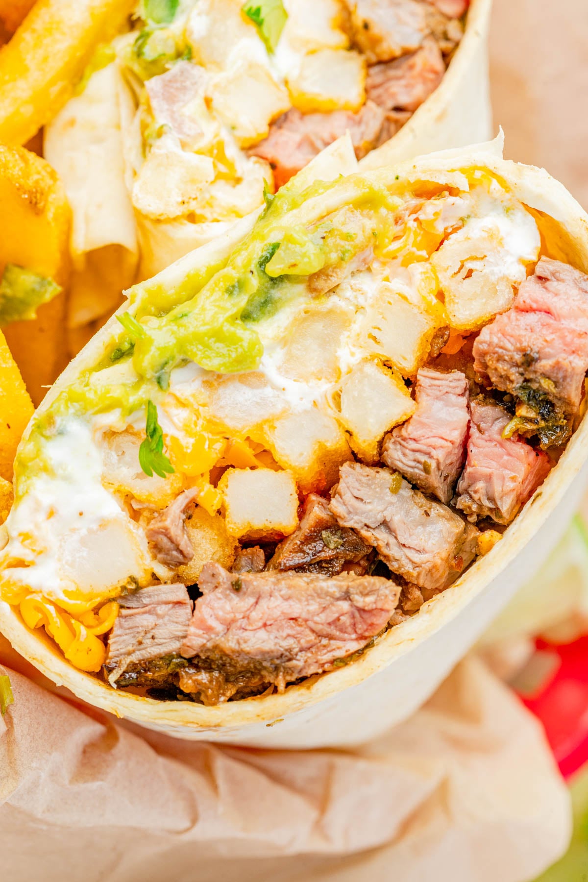 A close-up of a burrito cut in half, showing steak, cheddar cheese, guacamole, sour cream, and potato pieces in a flour tortilla.