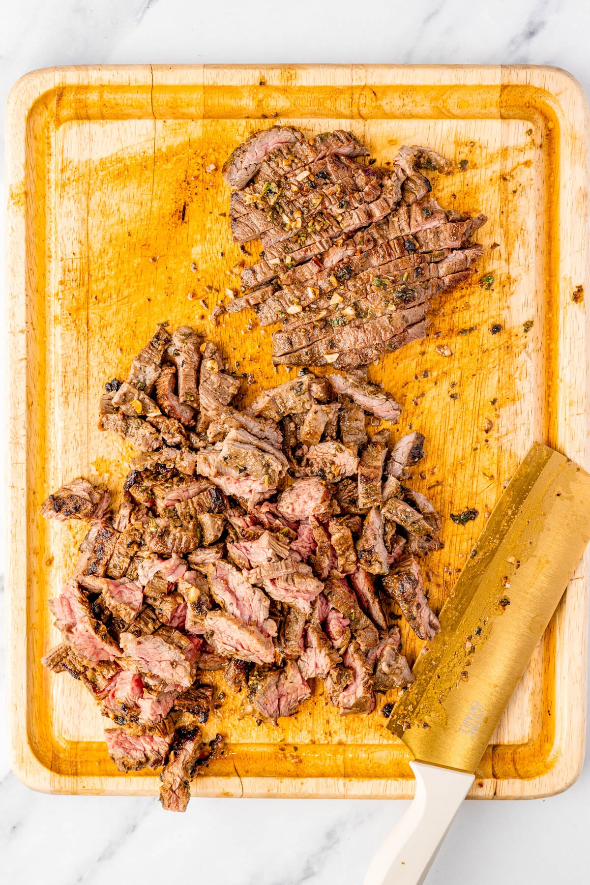 Sliced and chopped cooked steak on a wooden cutting board with a knife beside it.