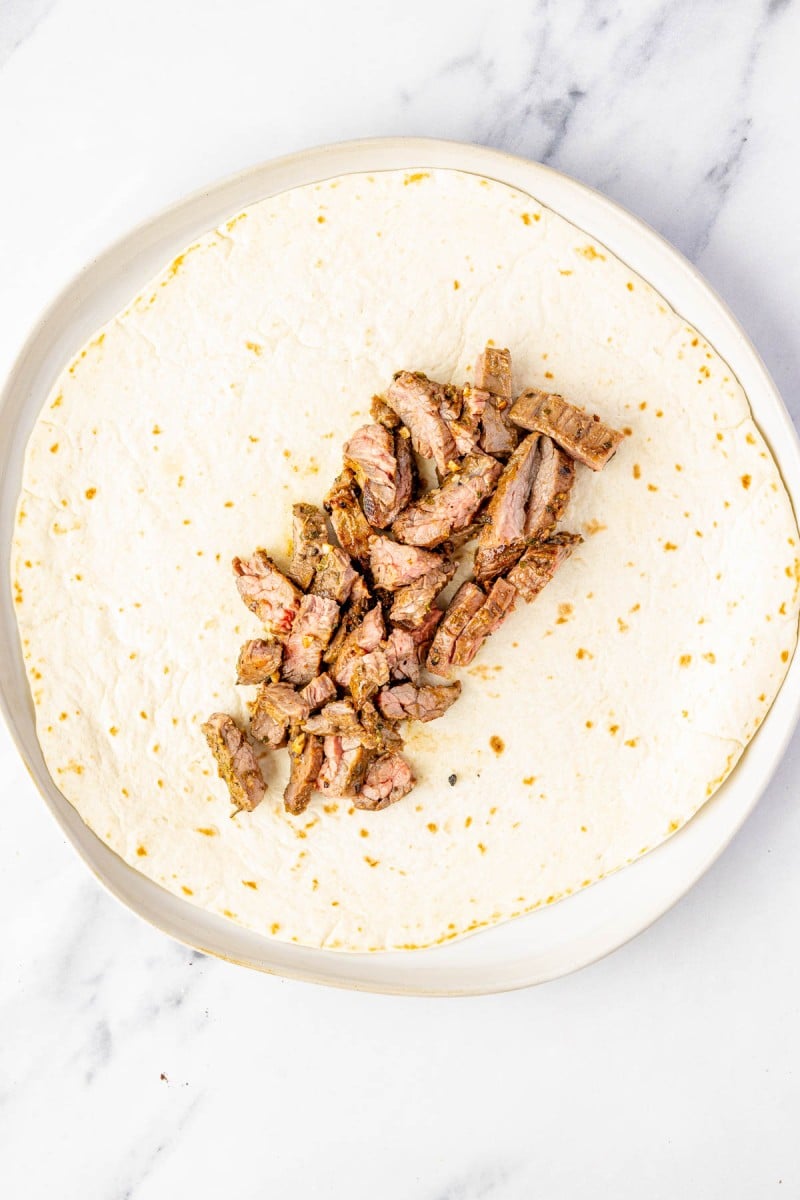 A flour tortilla on a plate with a pile of cooked steak strips placed in the center.