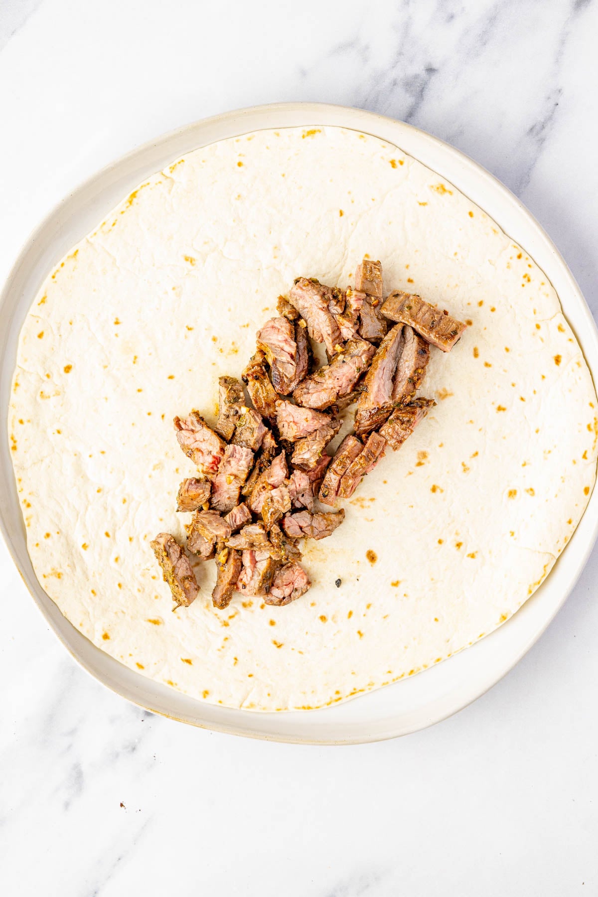 A flour tortilla on a plate with a pile of cooked steak strips placed in the center.