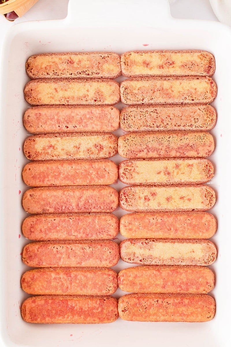 A baking dish filled with two layers of ladyfinger cookies arranged neatly side by side, slightly soaked and ready for the next recipe step.