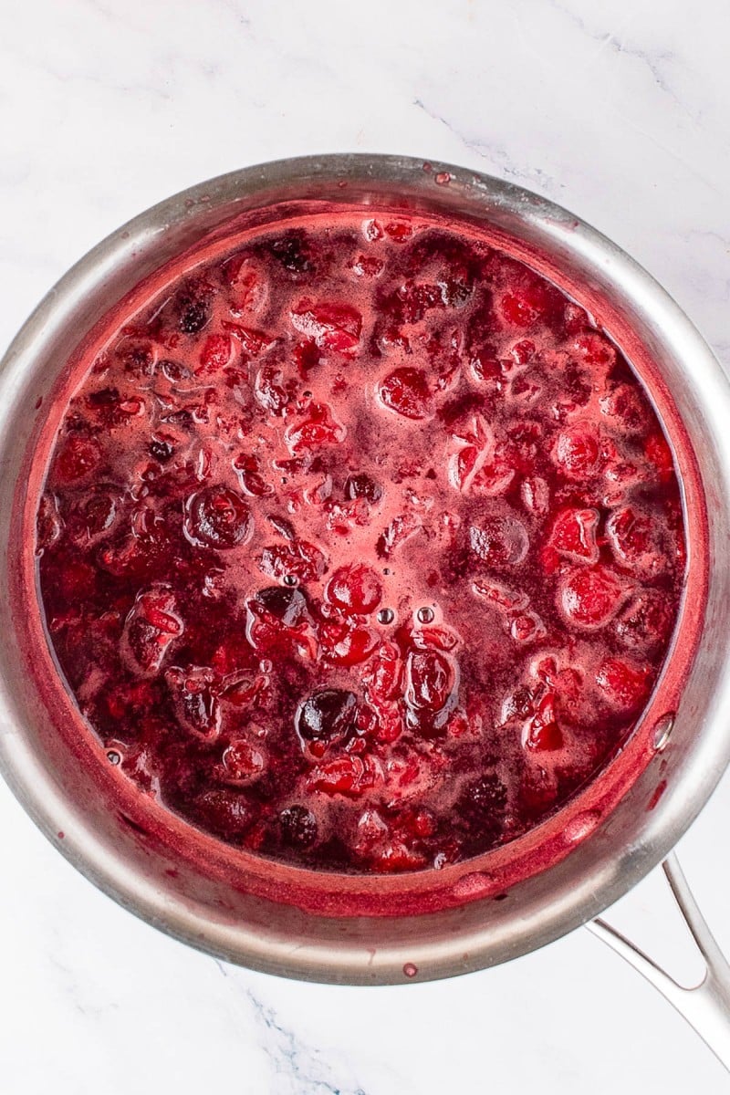 A stainless steel pot filled with simmering cranberry sauce, showing whole cranberries and thick red liquid.