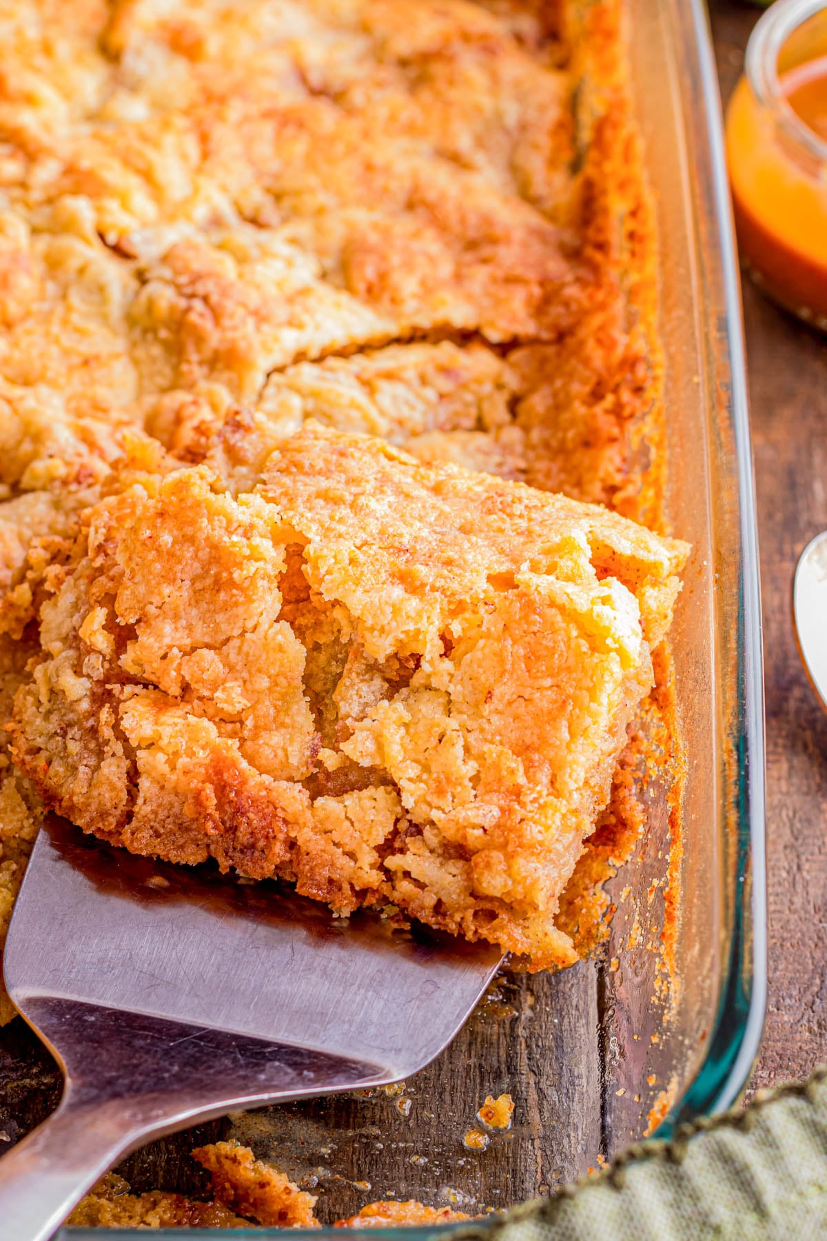 A close-up of a golden-brown cobbler being served from a glass baking dish using a metal spatula.